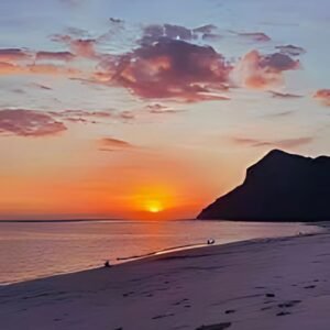 Matahari terbenam di Pantai Maluk depan pharadis hotel dengan langit berwarna oranye dan ungu, di tengah suasana tenang dan pemandangan pegunungan.
